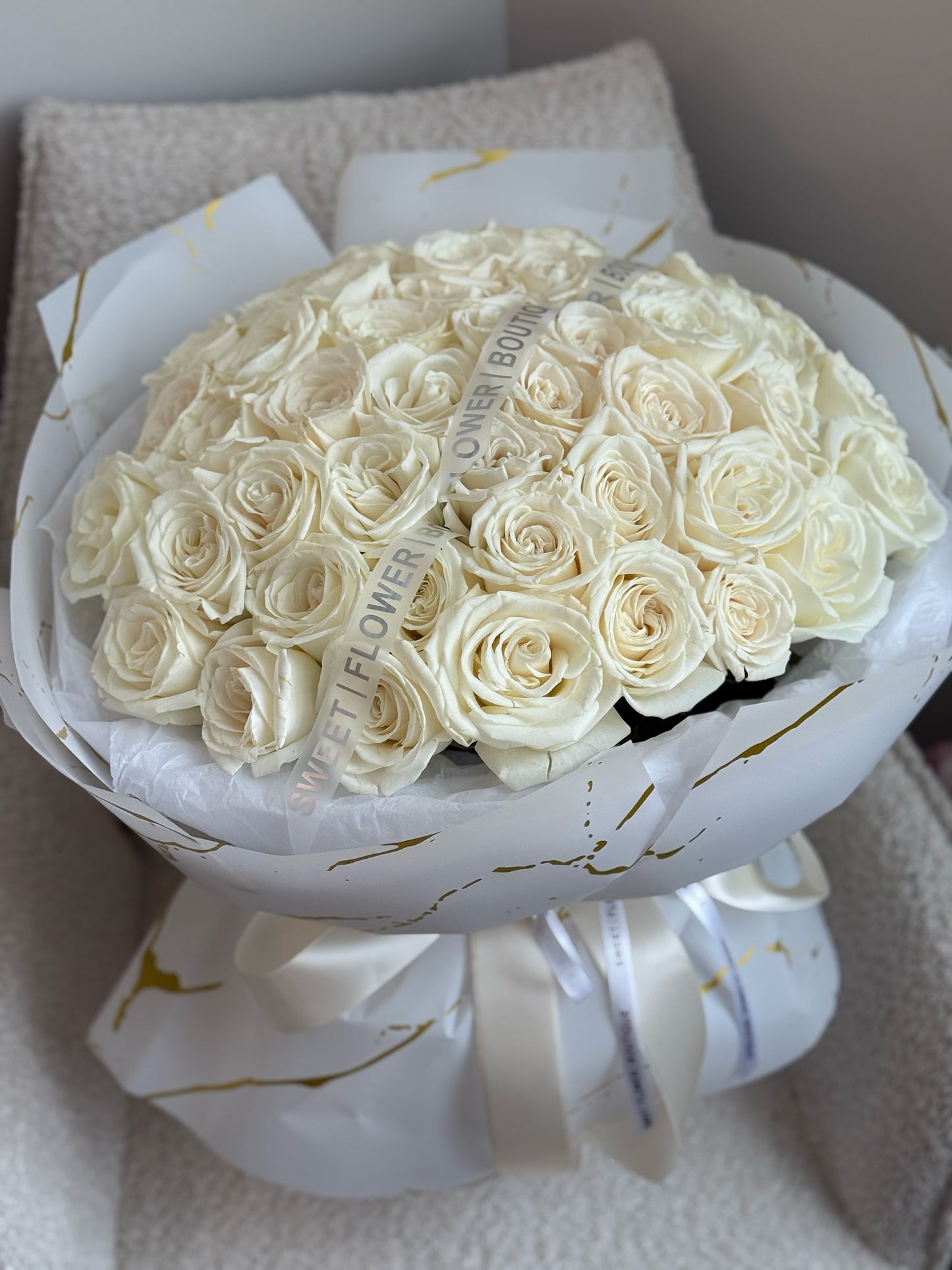 Close-up of fifty white roses arranged in a full round bouquet with satin ribbons