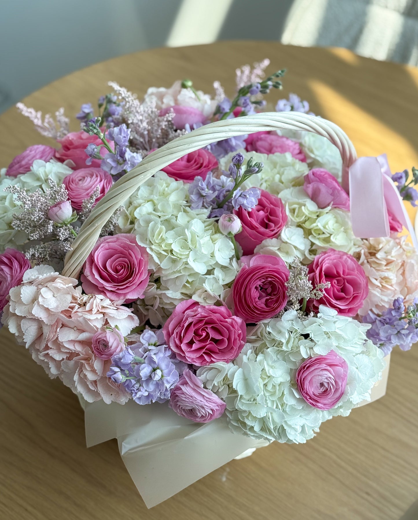 Basket of flowers with pink and white roses on a wooden surface