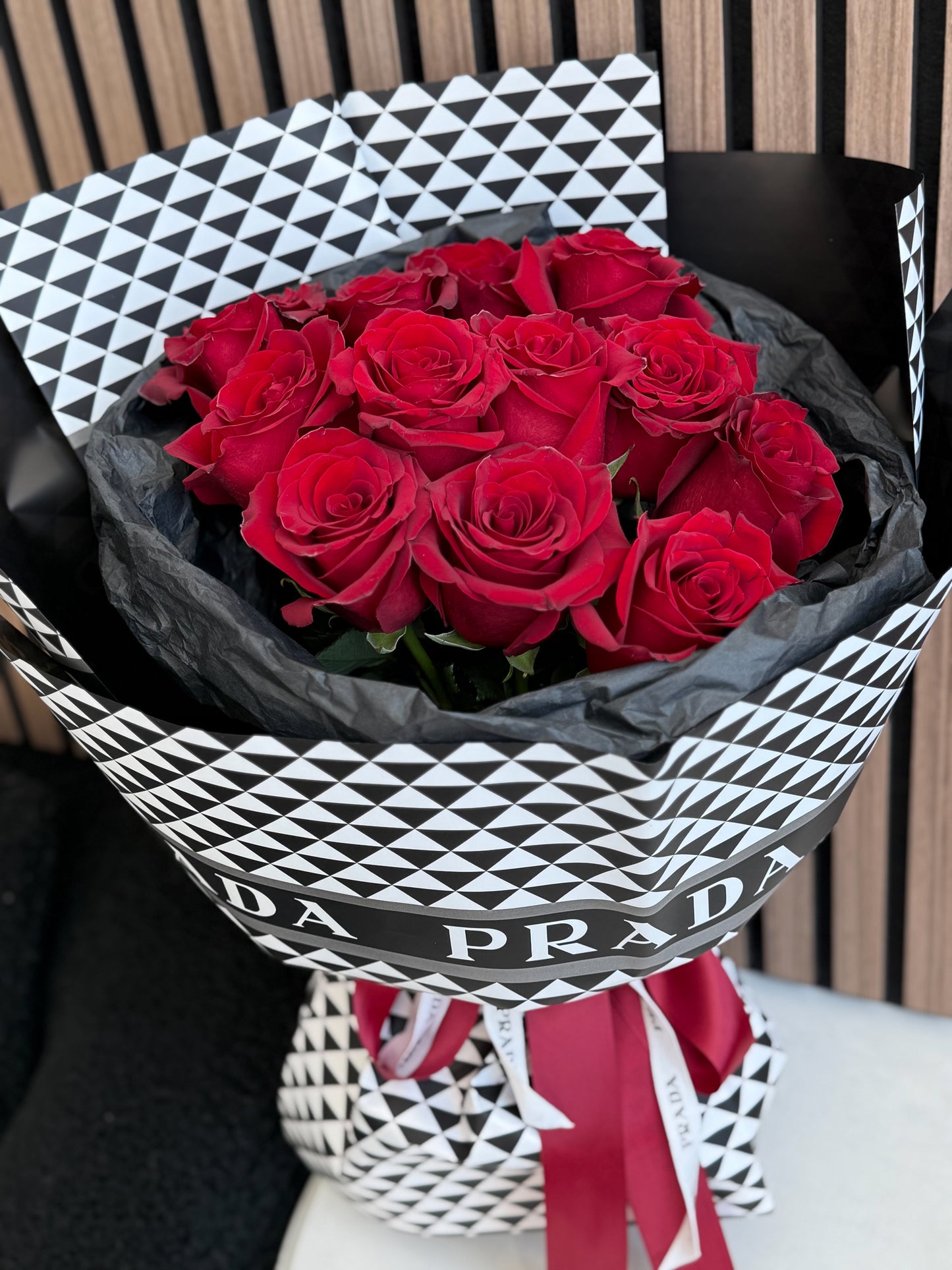 Bouquet of red roses wrapped in black paper with Prada branding.
