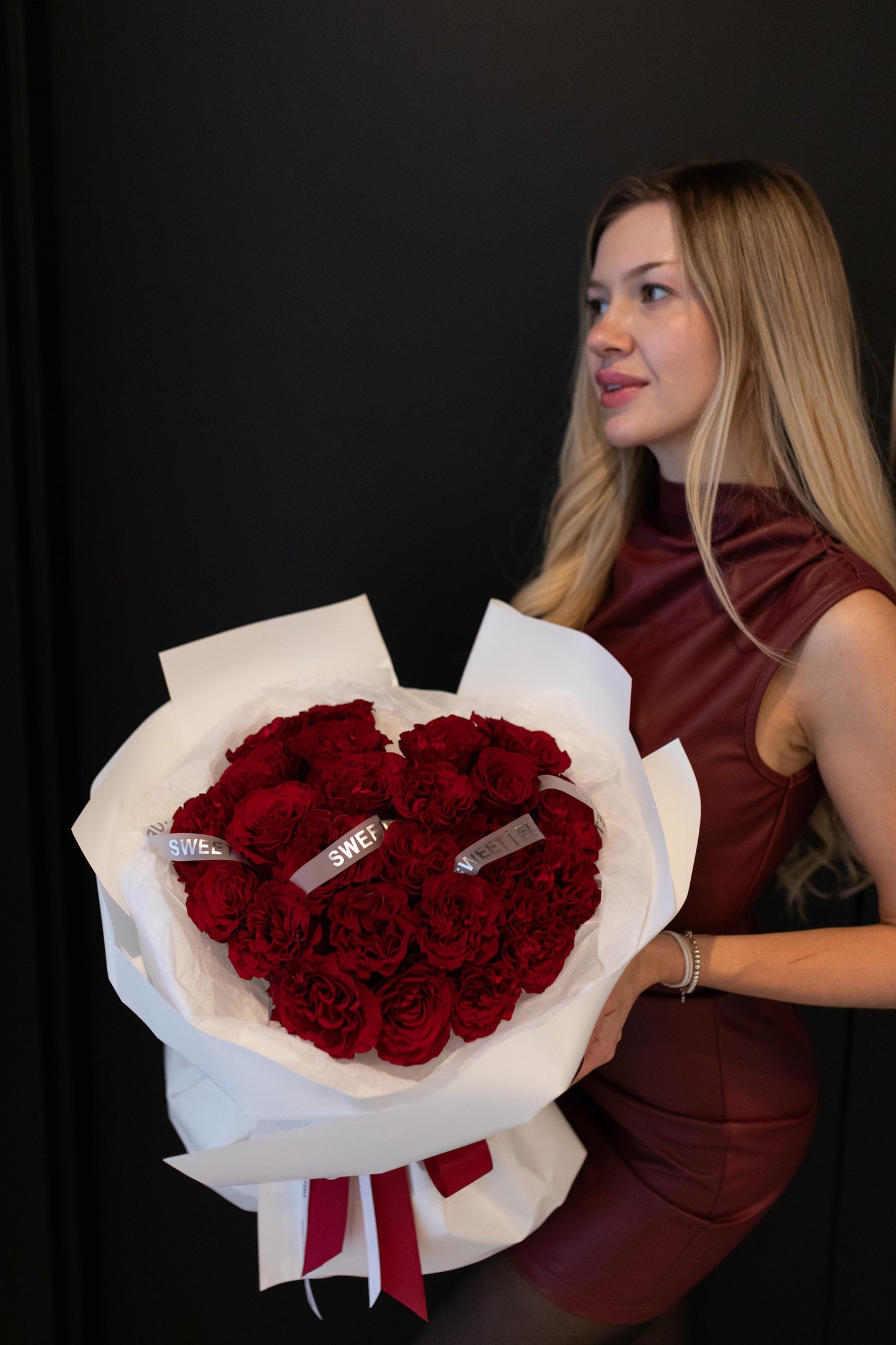 Woman holding a large bouquet of red roses with white wrap and ribbons against a black background