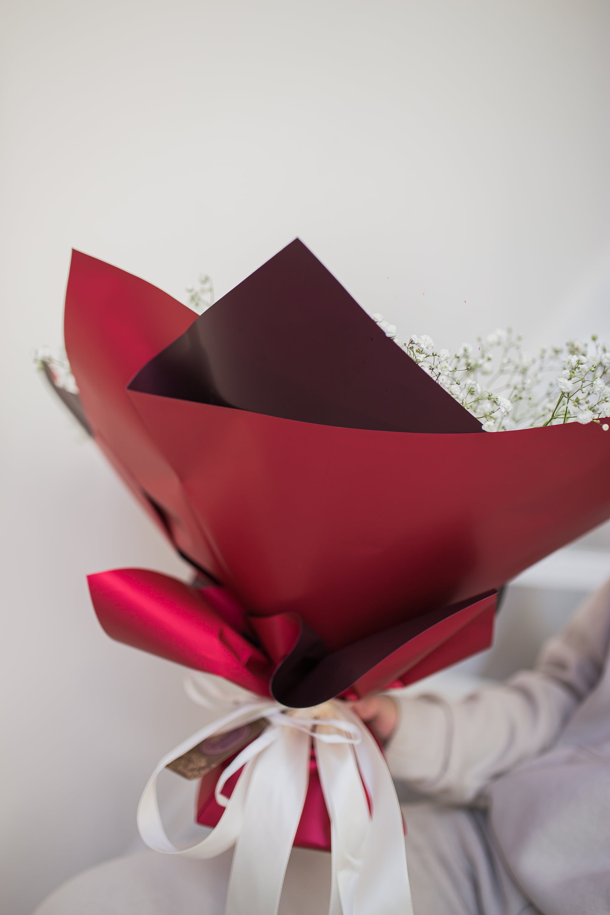 Holding a bouquet in red and purple paper wrap with white ribbon