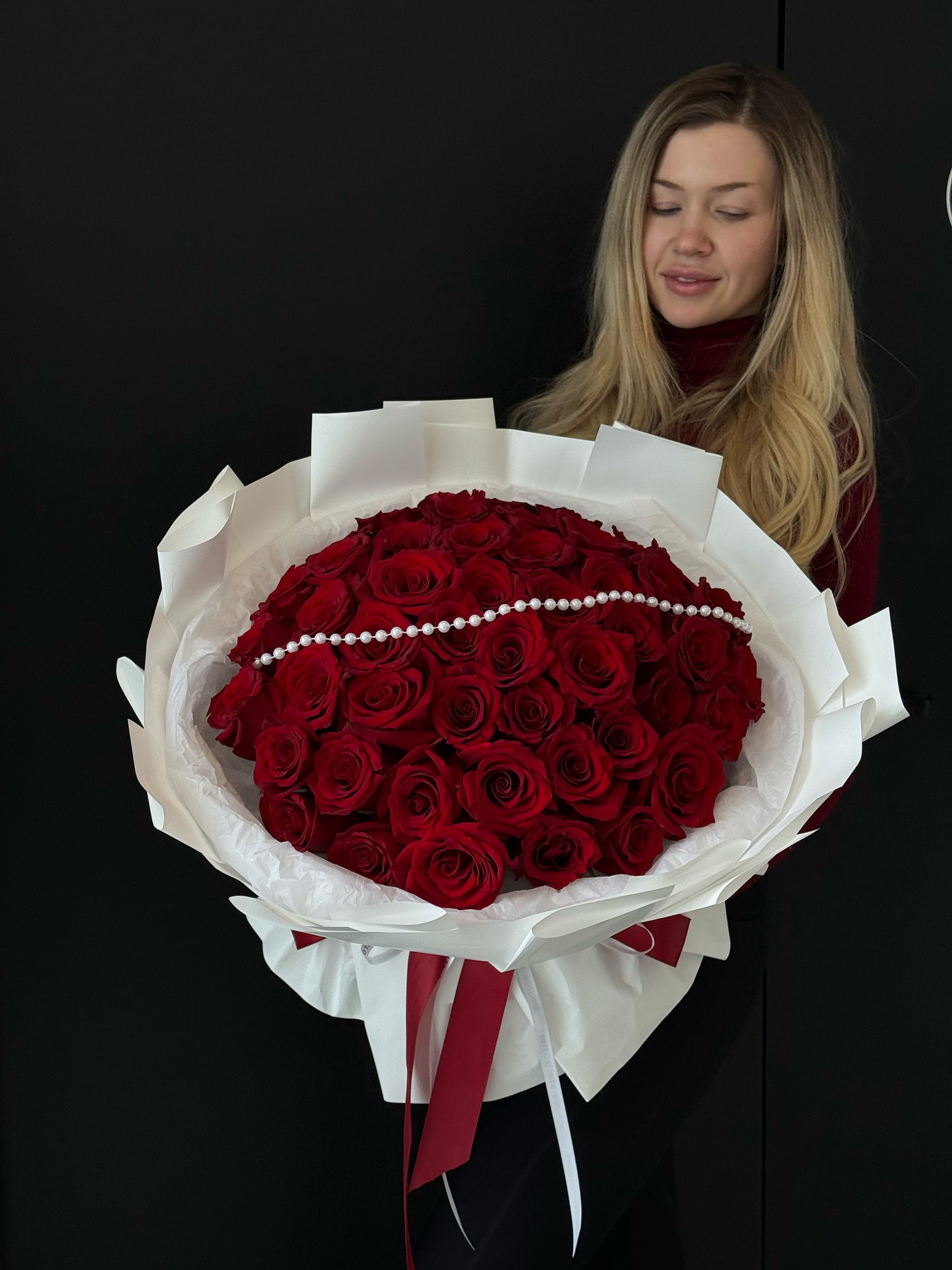 Woman holding a large bouquet of red roses against a black background
