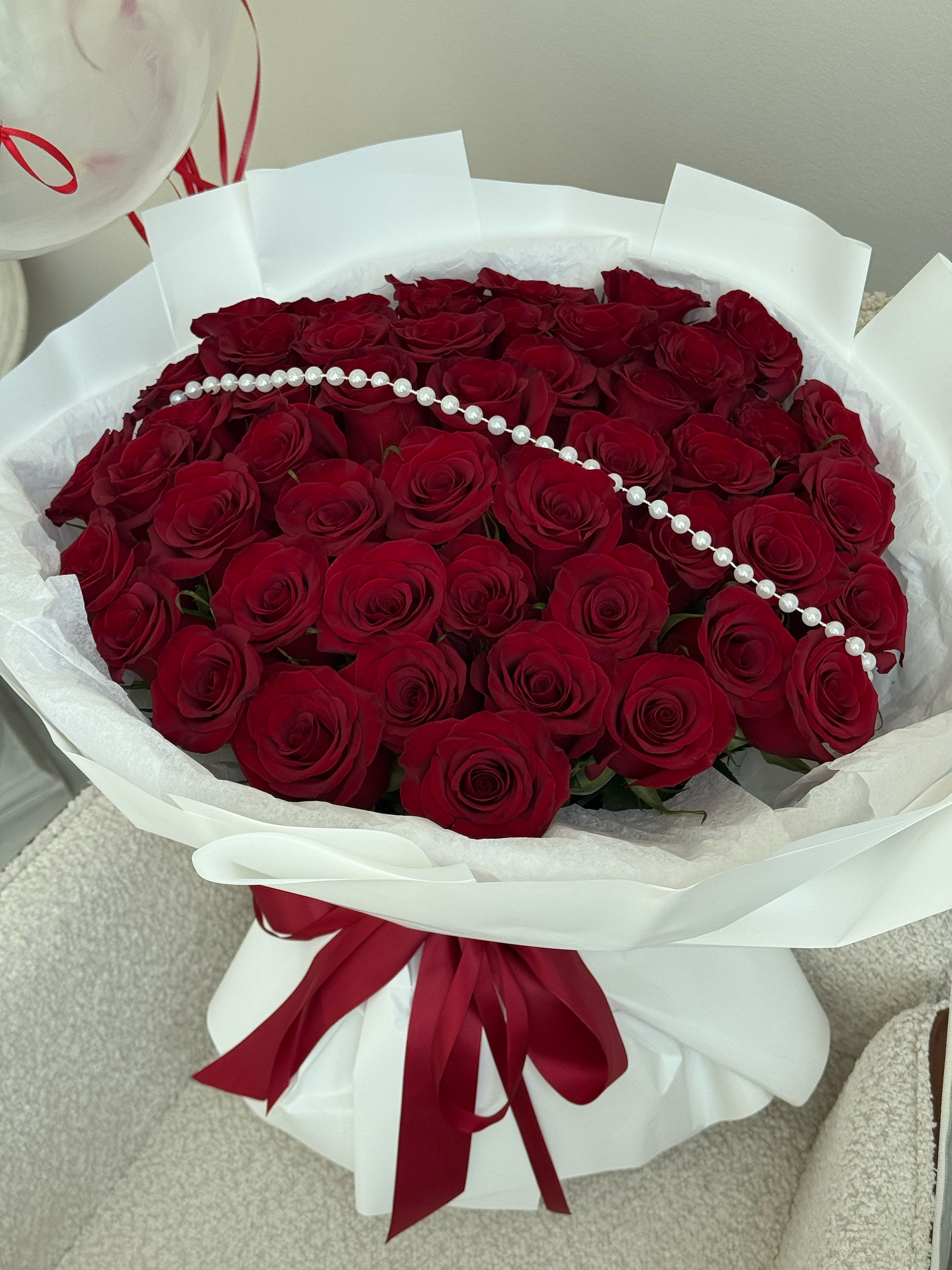 Bouquet of red roses with a pearl necklace and red ribbon on a neutral background