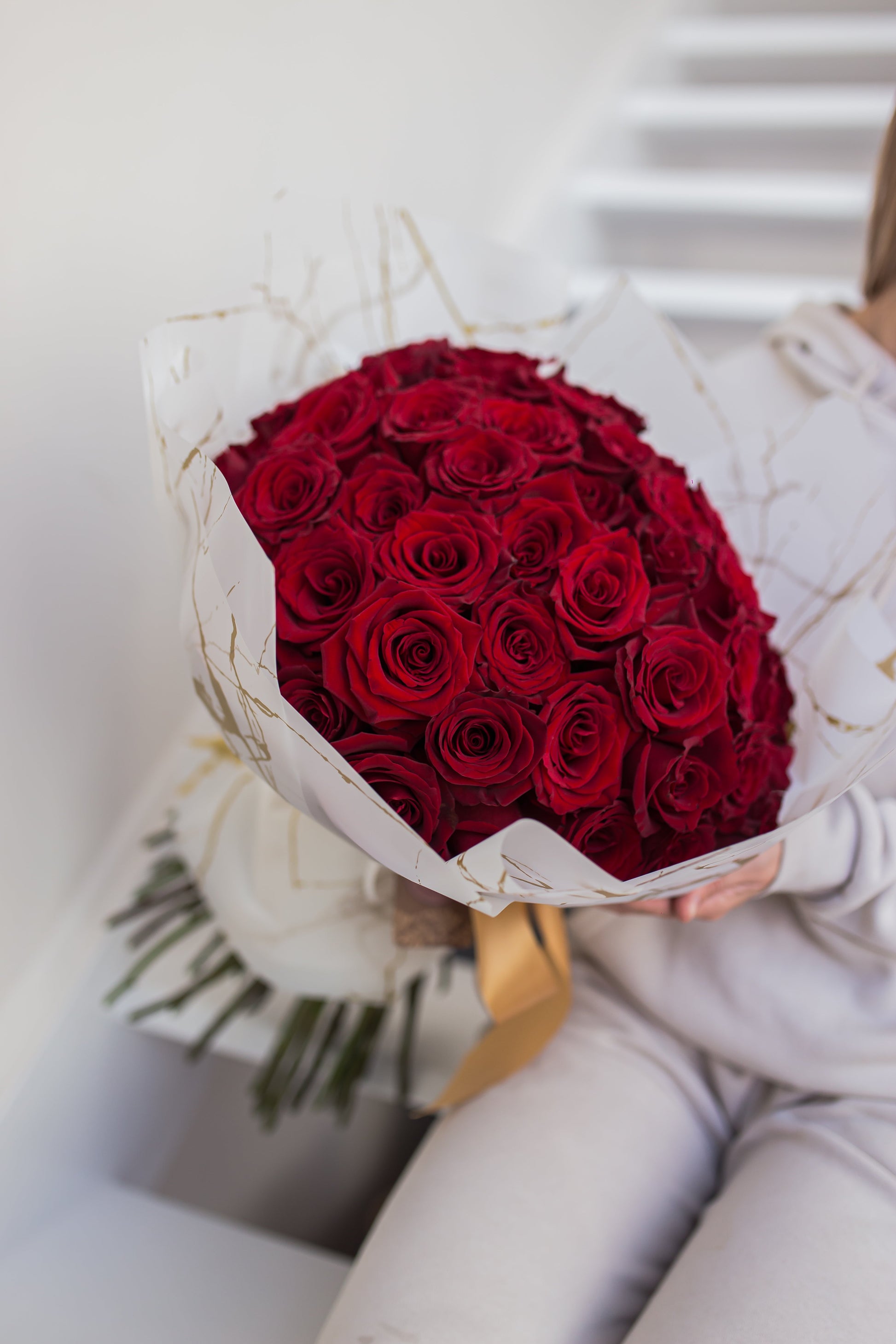 A person holding a bouquet of premium red roses wrapped with waterproof paper and silky ribbon.