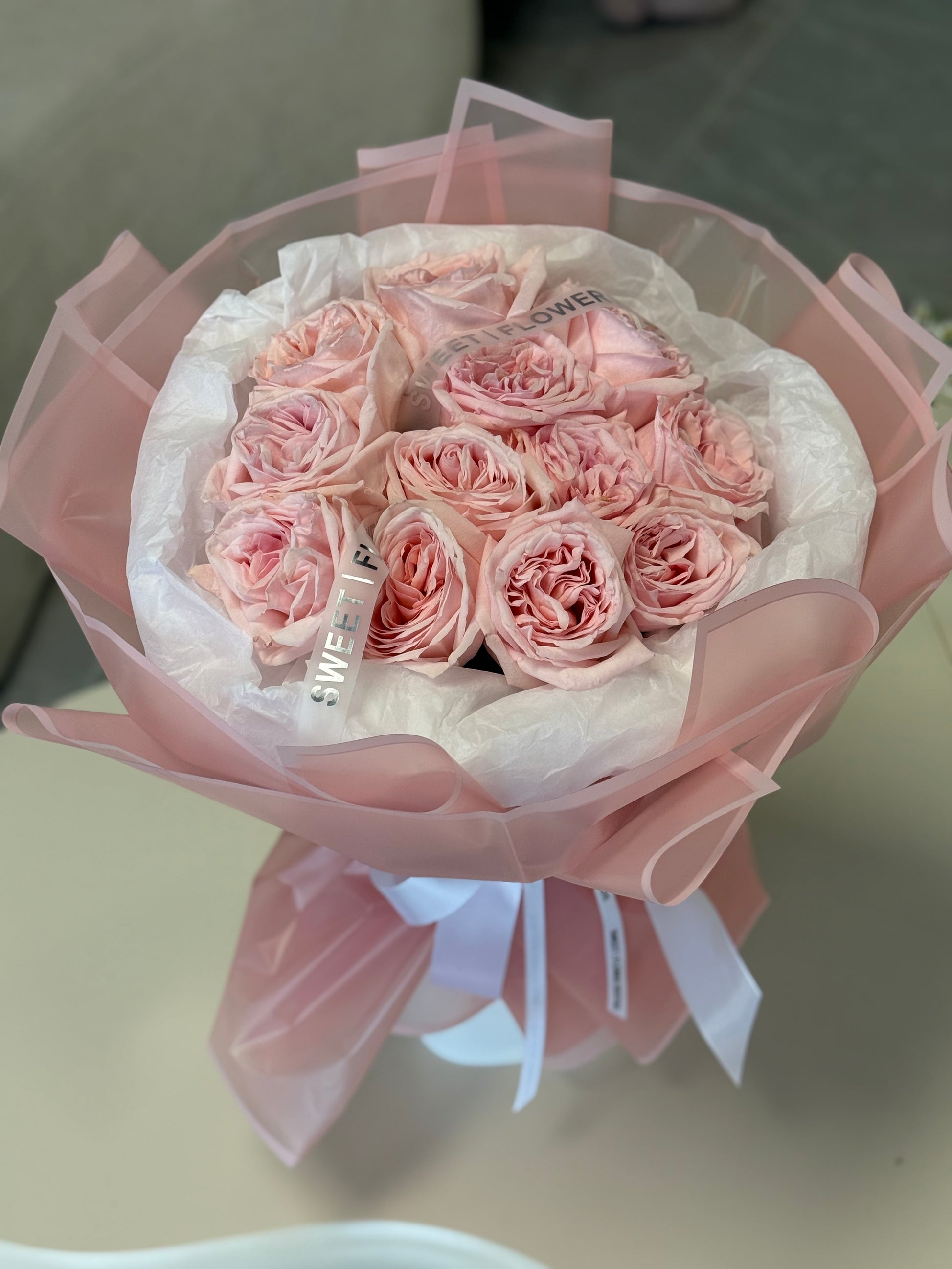 Bouquet of pink roses wrapped in white paper with a pink bow on a light surface.