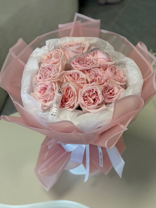 Bouquet of pink roses wrapped in white paper with a pink bow on a light surface.