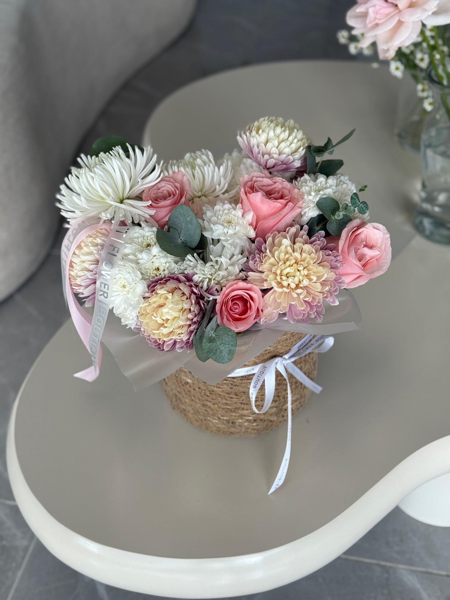 Bouquet of flowers on a small stand with a pink ribbon on a gray surface.