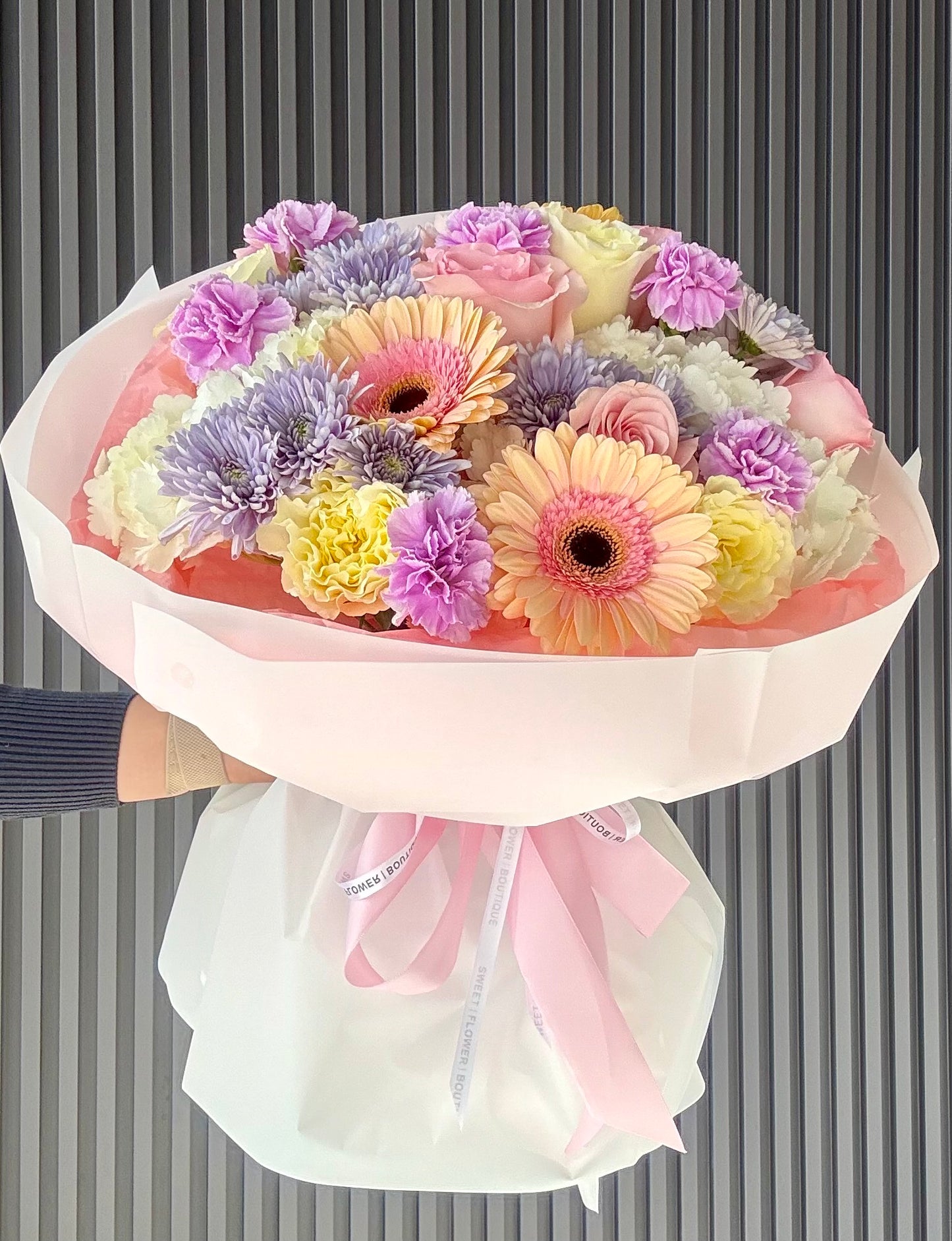Bouquet of colorful flowers wrapped in pink paper against a striped background