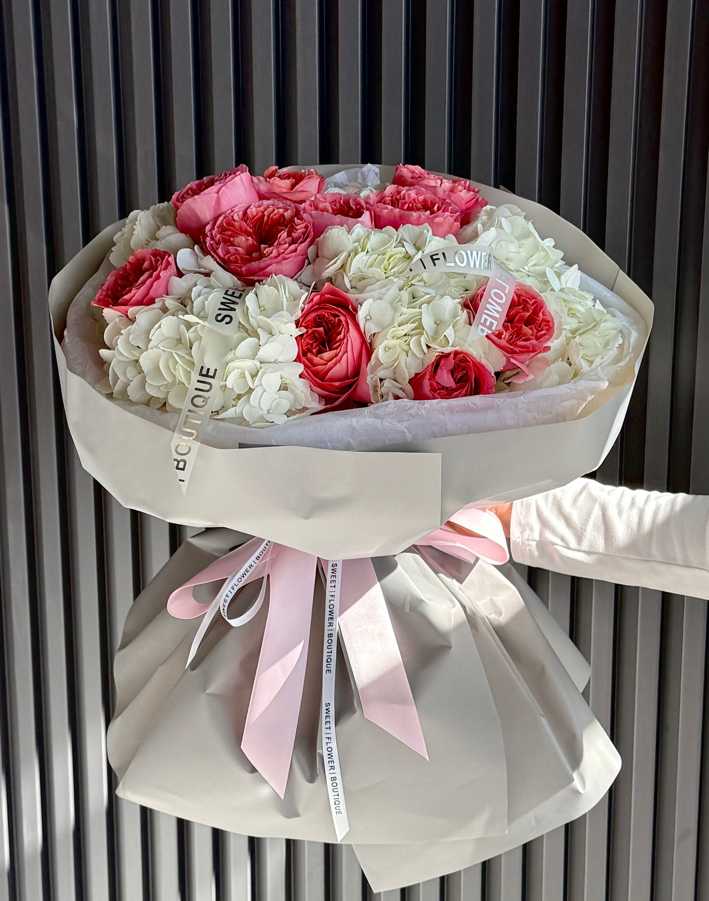 Bouquet of pink and white flowers with decorative ribbons against a neutral background