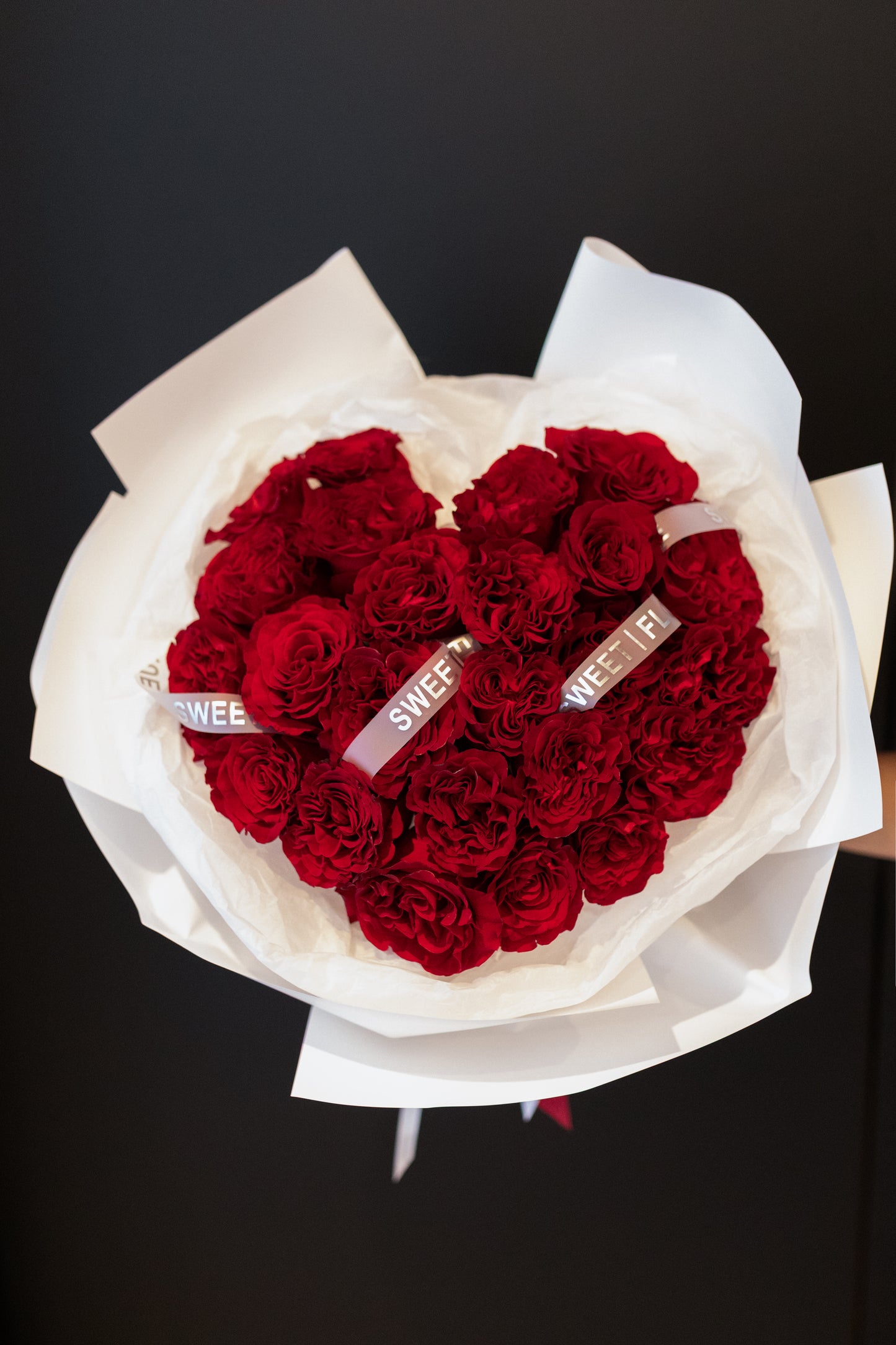 Heart-shaped bouquet of red roses with 'SWEET' ribbons on a black background