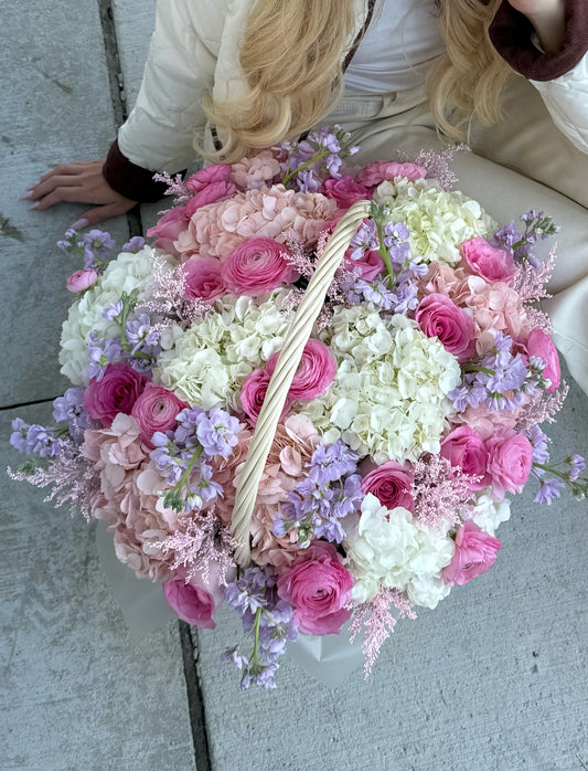 Large bouquet of pink, white, and purple flowers with a basket in the center on a concrete surface.