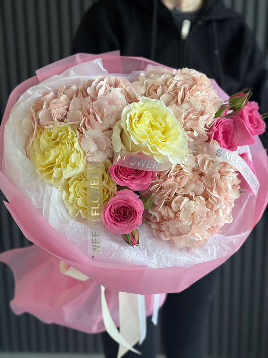 Bouquet of pink, yellow, and white flowers with a pink wrap held by a person.