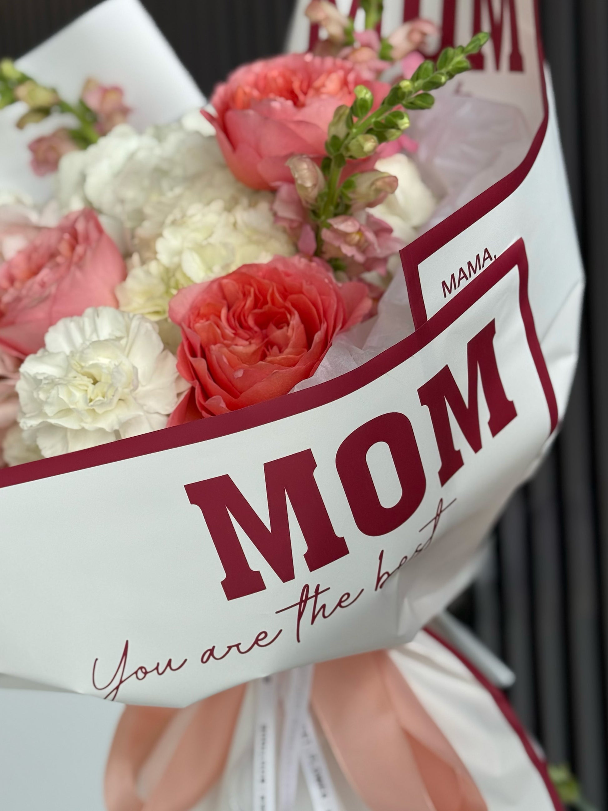 Bouquet of flowers with a card that reads 'MOM You are the best' on a white background.