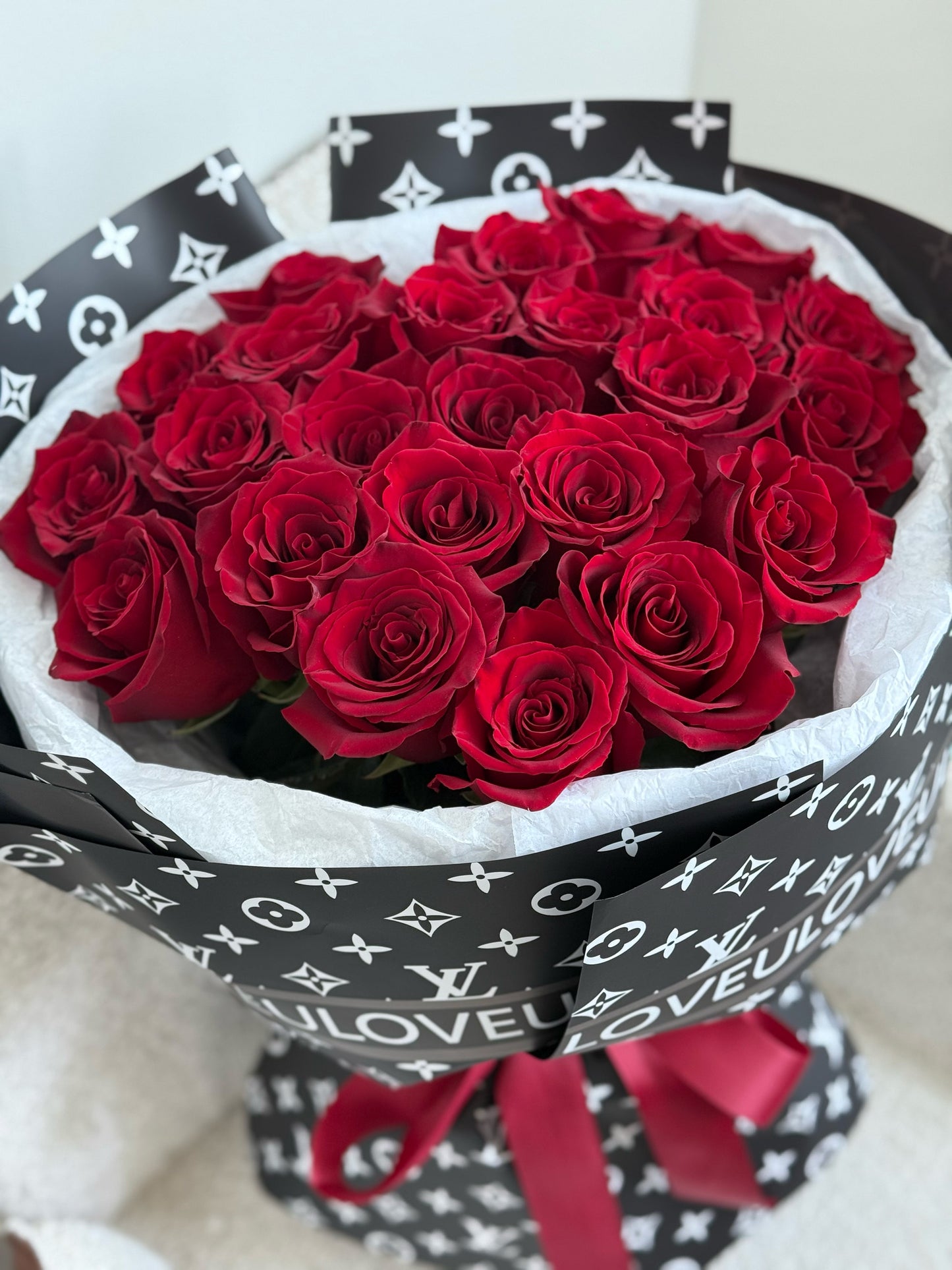 Bouquet of red roses wrapped in a Louis Vuitton-themed paper with a red ribbon.