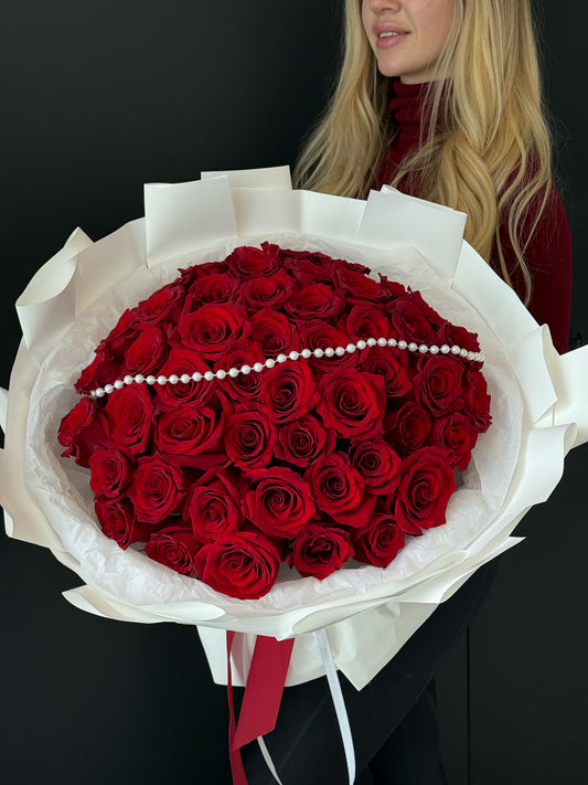 Bouquet of red roses with a white wrap held by a person against a black background