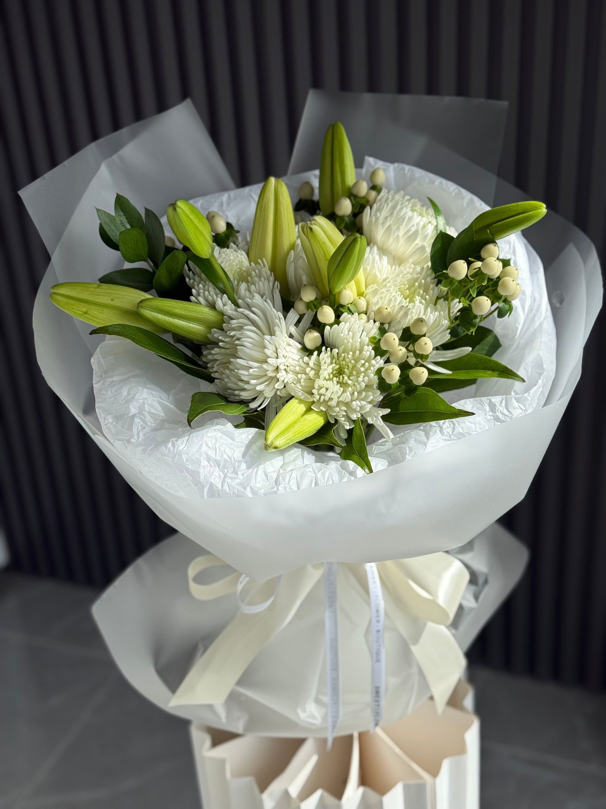 White lily and chrysanthemum bouquet with green accents wrapped in translucent paper, available for same-day delivery.