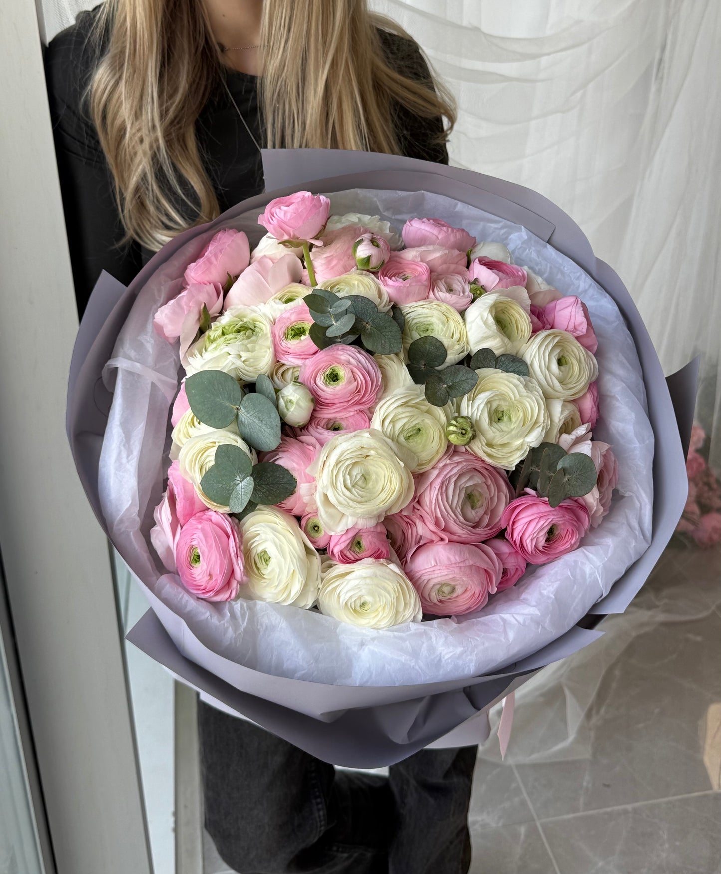 Bouquet of pink and white ranunculus with eucalyptus held by a person.