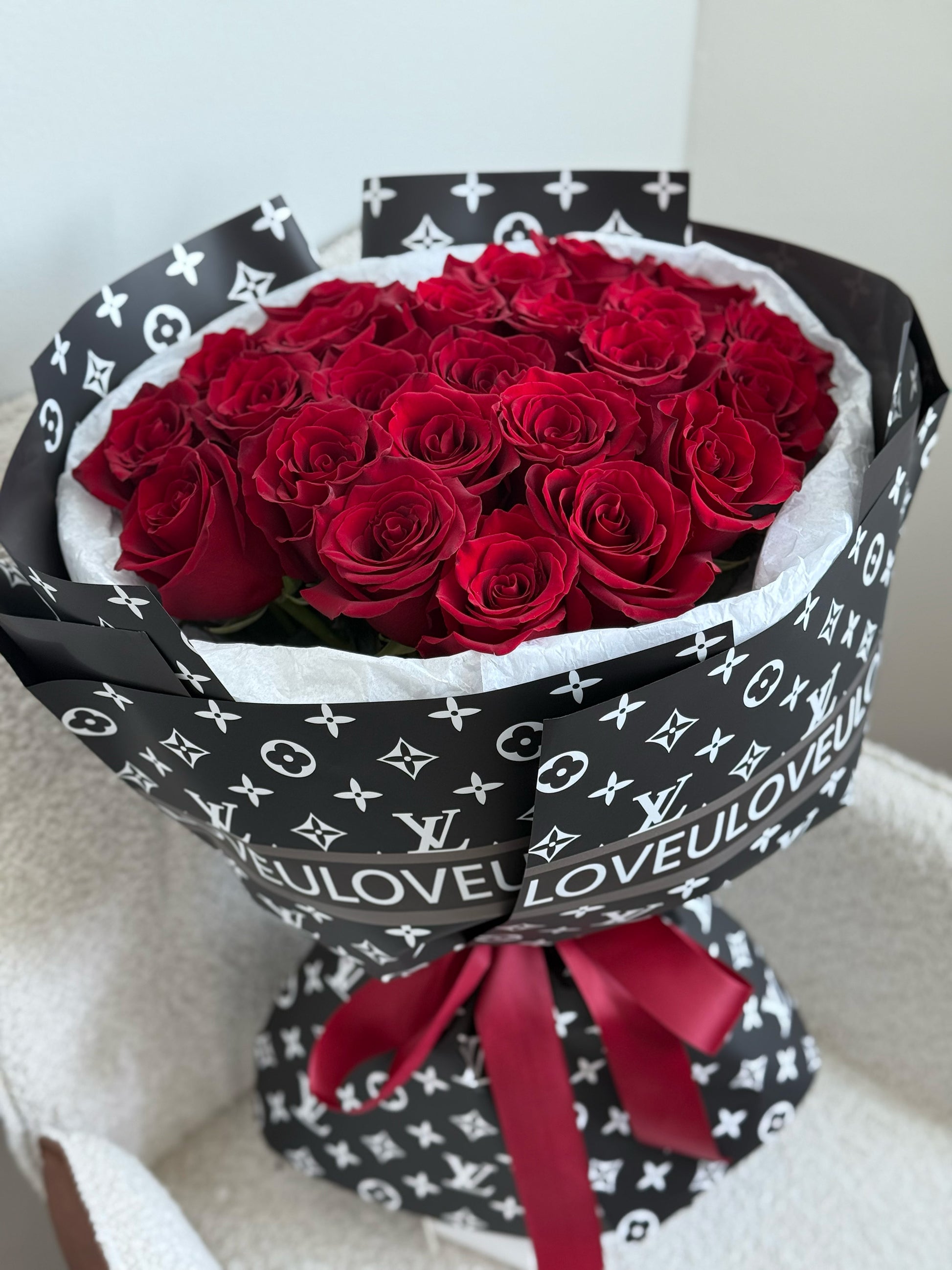 Bouquet of red roses wrapped in black Louis Vuitton-patterned paper with a red ribbon.