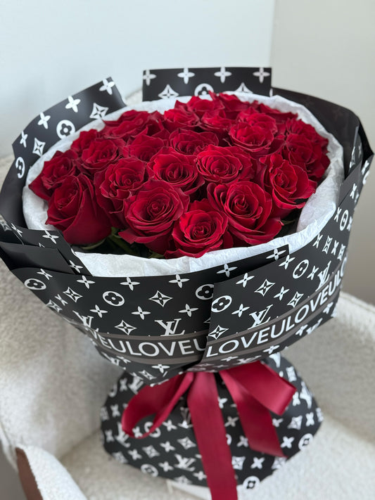 Bouquet of red roses wrapped in black Louis Vuitton-patterned paper with a red ribbon.