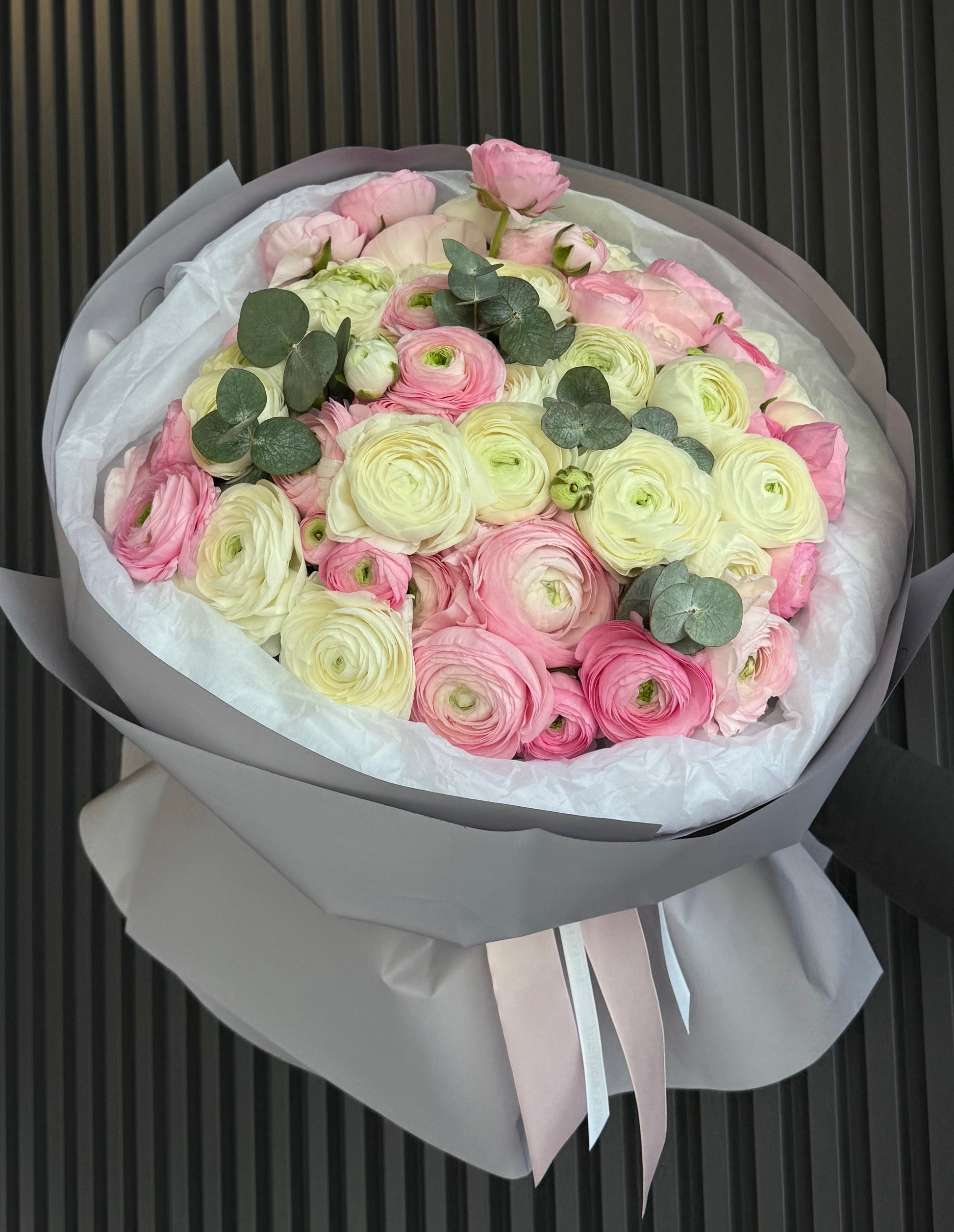 Bouquet of pink and white flowers with green leaves in a gray box on a dark background